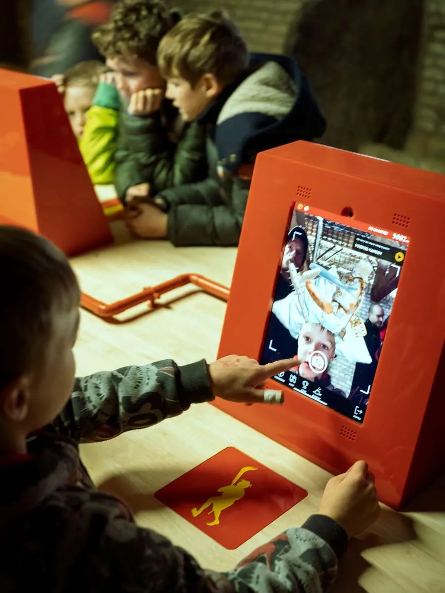 Kinderen spelen aan rode speelstations met een gele figuur op een kaart.