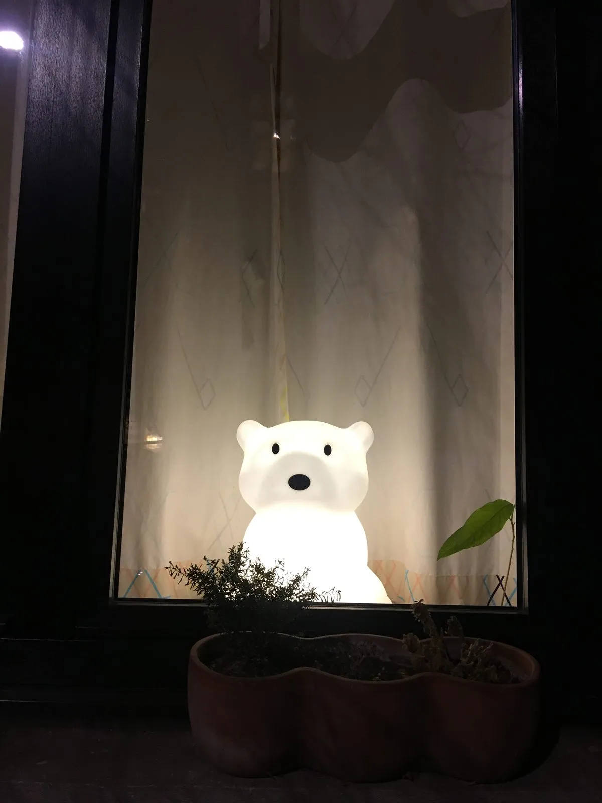 Een verlicht berenlampje van een kind staat achter het raam mee te spelen.