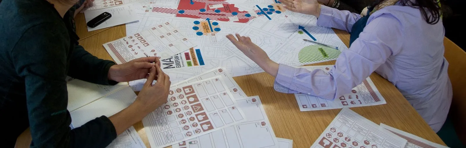 Handen rond een tafel vol kaarten en stickervellen tijdens een mappingsessie.