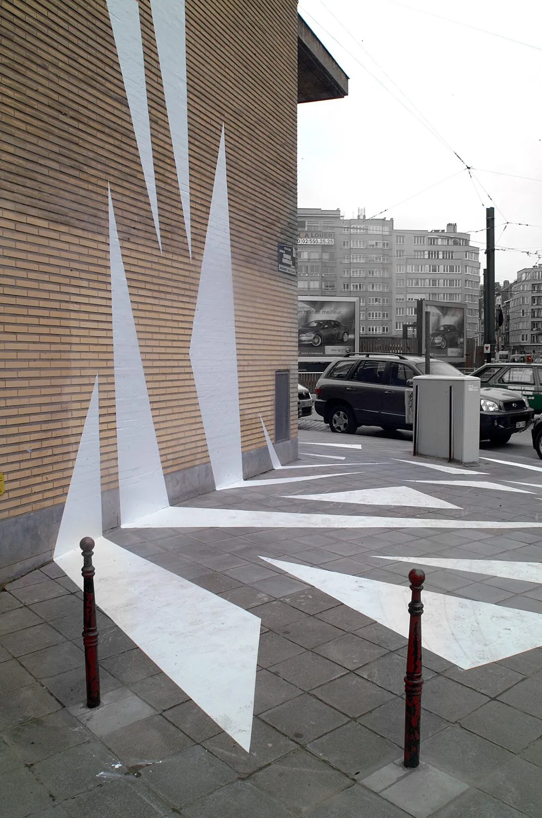 Een zebrapad van witte stickers loopt van de stoep de hoek om en versplintert omhoog over een bakstenen gevel.