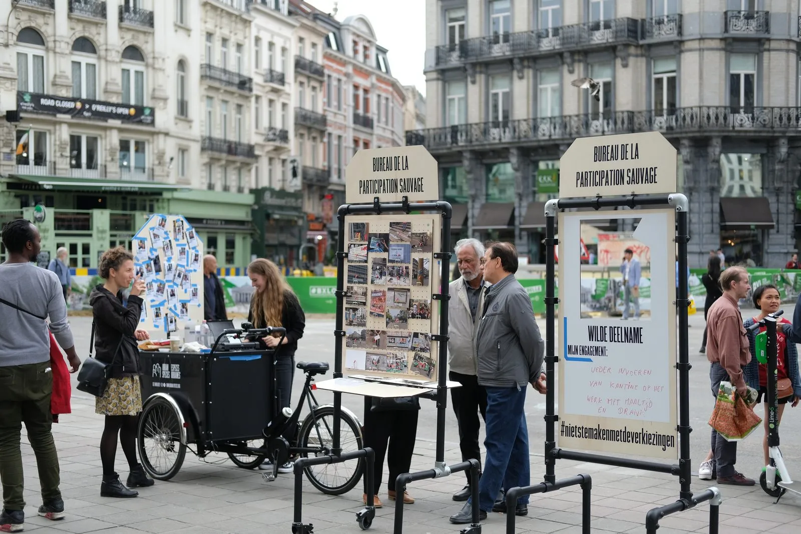 Het Bureau de la participation sauvage op het Beursplein: twee mobiele modules met fotoborden en een bakfiets, met voorbijgangers in gesprek.