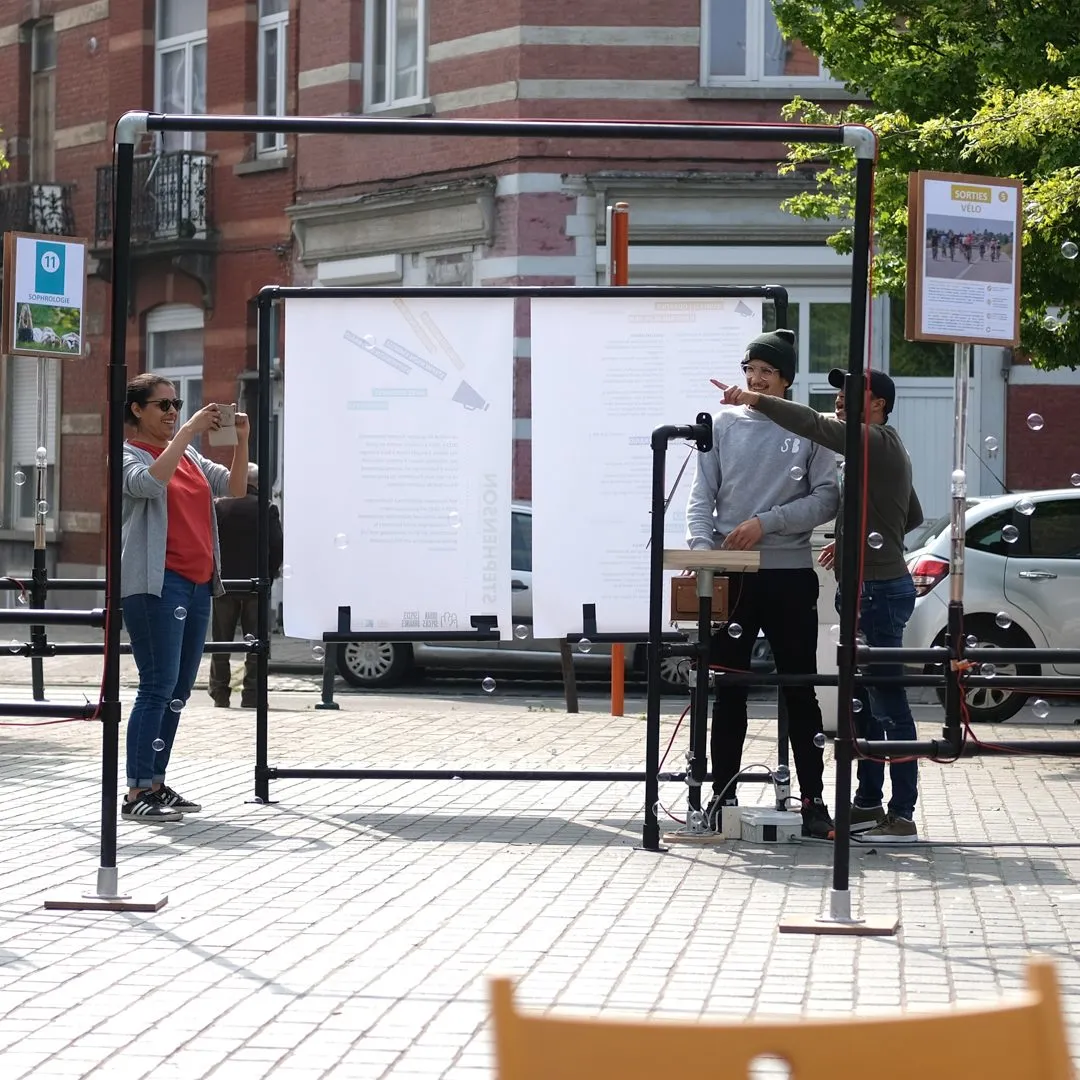 Een buizenframe met een groot affiche op straat, waar deelnemers bij staan en fotograferen.