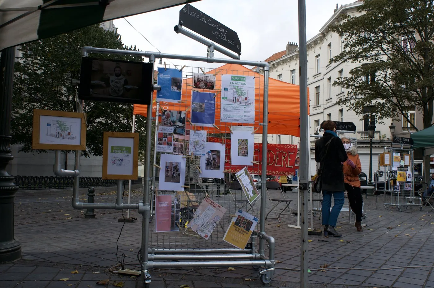 Bij valavond staan meerdere frames met panelen en foto’s op een plein, verlicht door spots.