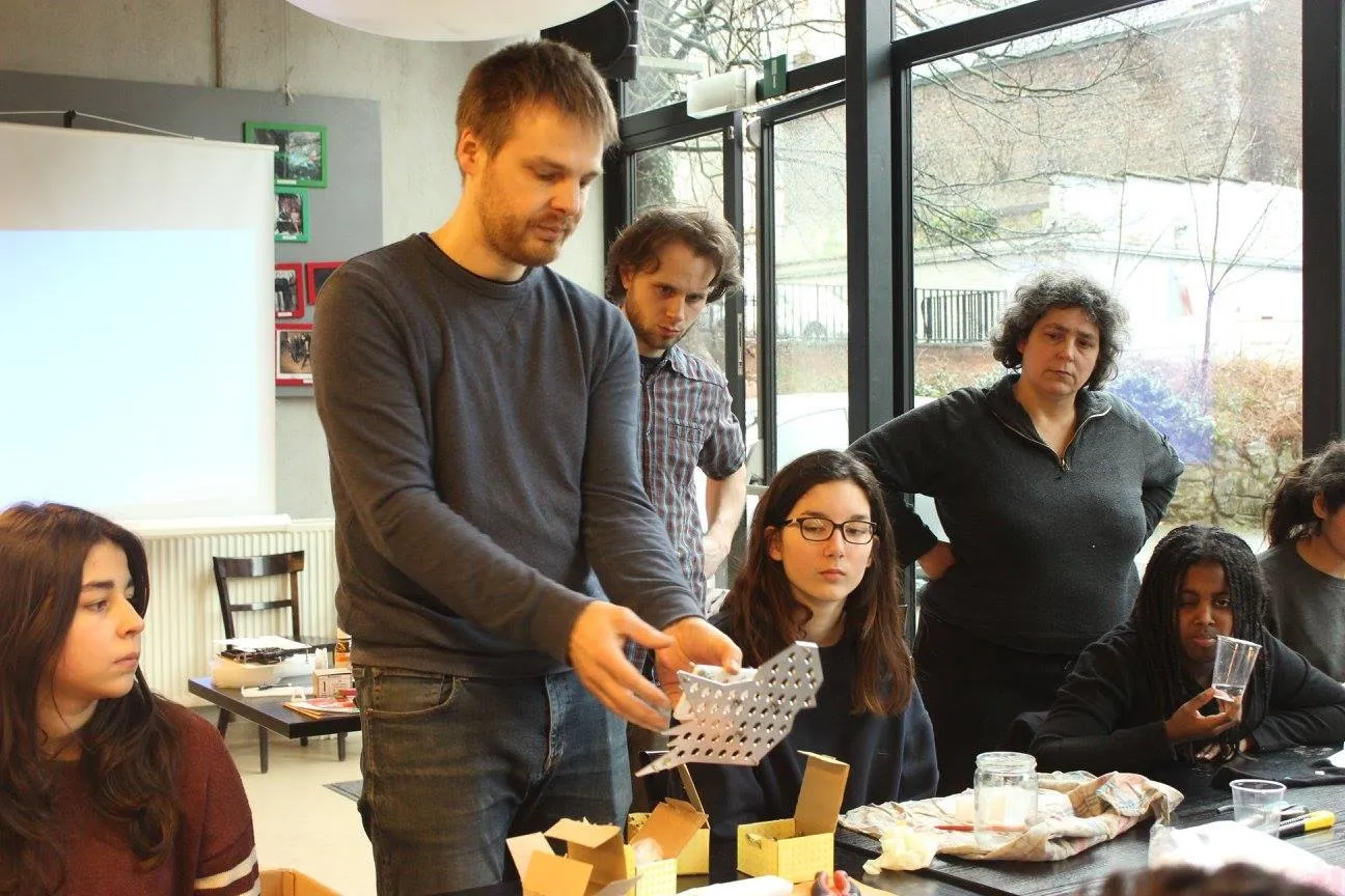 Thomas Laureyssens toont een uitgesneden paneel aan een groep deelnemers rond een werktafel.