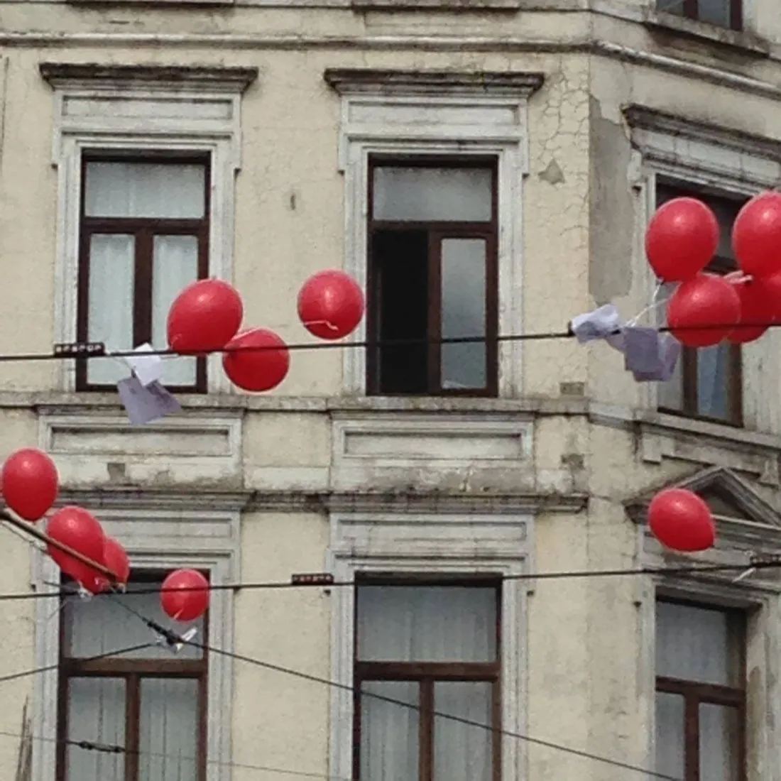 Rode ballonnen hangen aan draden voor de ramen van een Brusselse gevel.