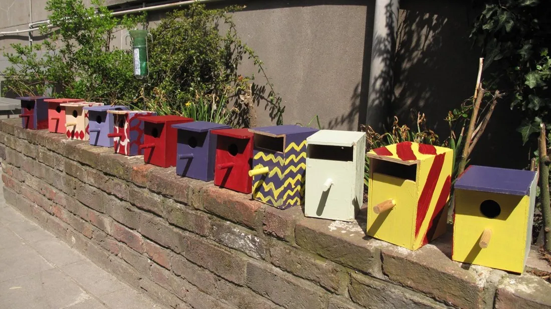 Een rij zelfgemaakte, felgekleurde vogelhuisjes op een lage tuinmuur.