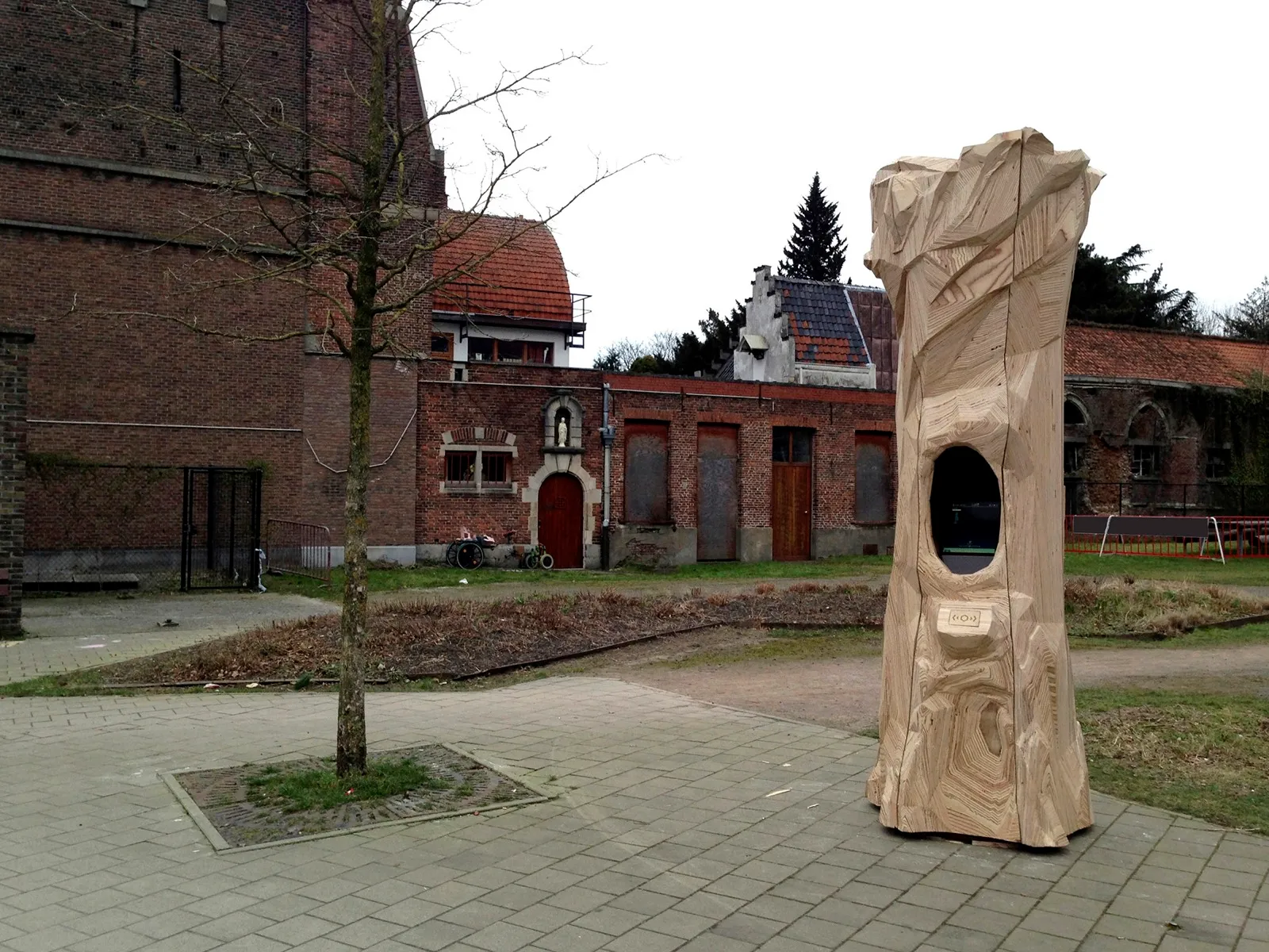 De houten ZWERM-totem, een uitgesneden boomstam met scherm, op een plein in de wijk.