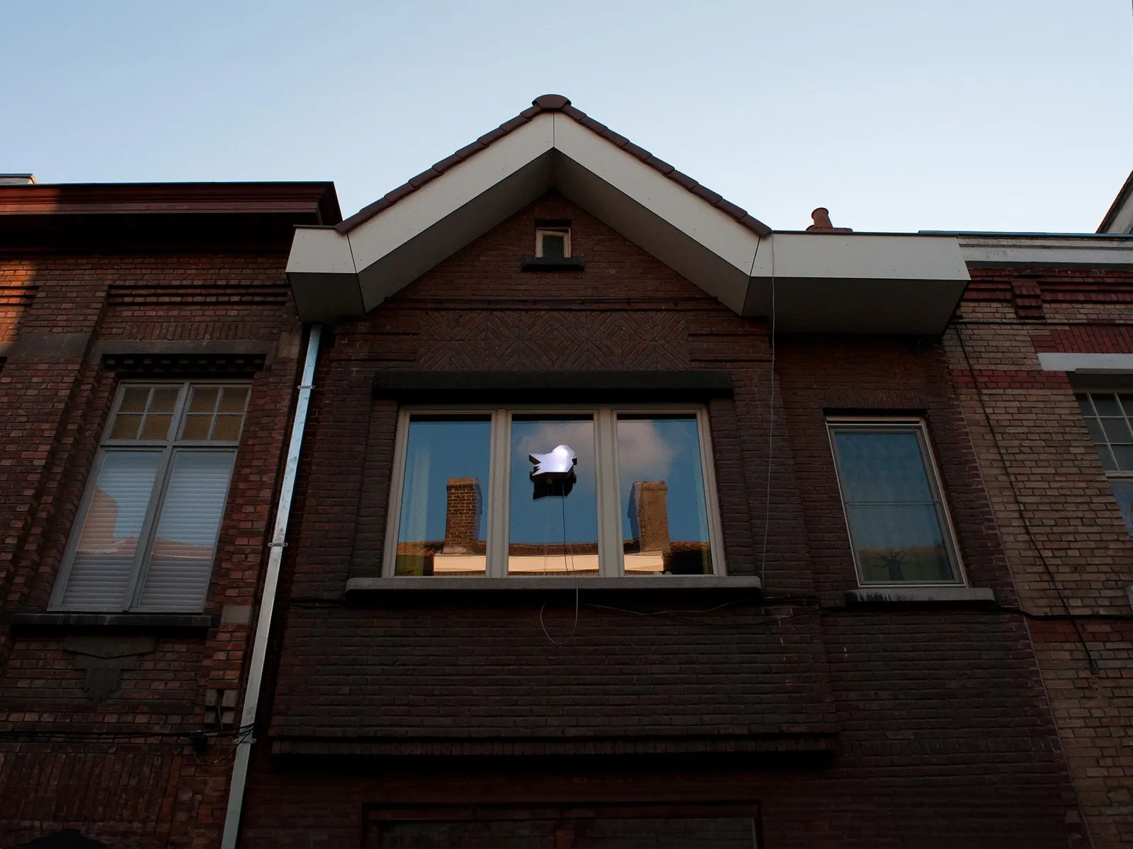 Een verlichte mus hangt voor een raam op een gevel, bij valavond.